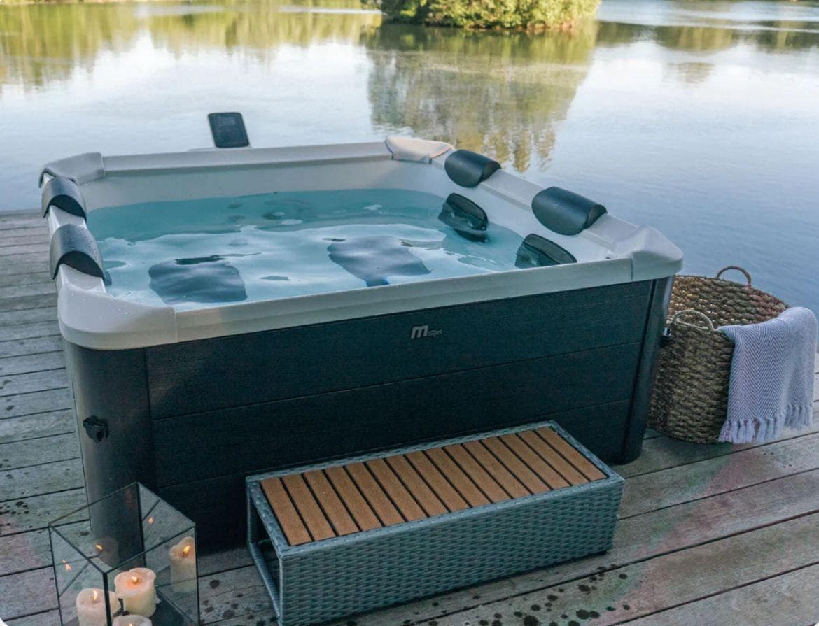 Spa estructural MSpa TRIBECA con acabado nogal oscuro sobre un deck de madera junto a un lago