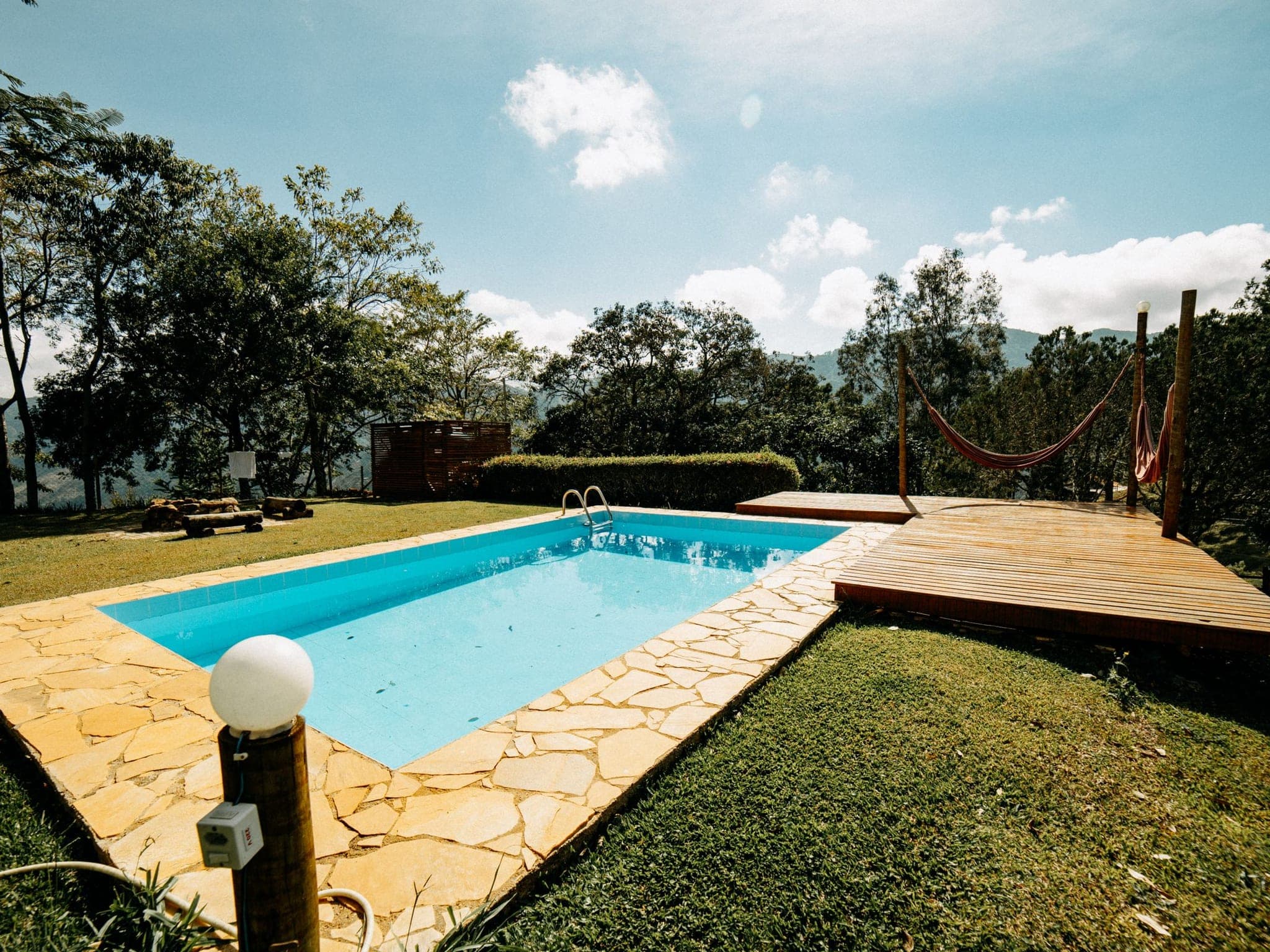 Piscina rectangular en un jardín, con borde de piedra y deck de madera con hamacas